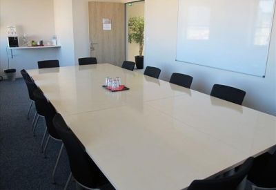 Spacious professional meeting room with a large white boardroom table and black chairs.