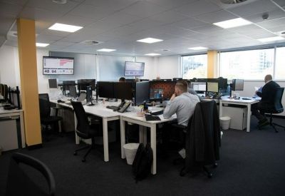 Open-plan office with multiple workstations, monitors, and large windows.