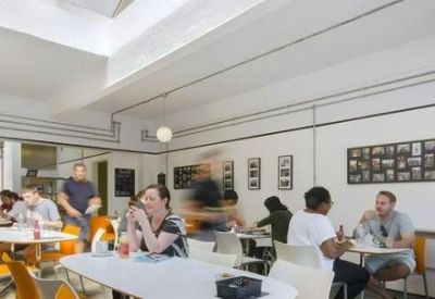 Light-filled communal cafe area with wooden furniture and people working.