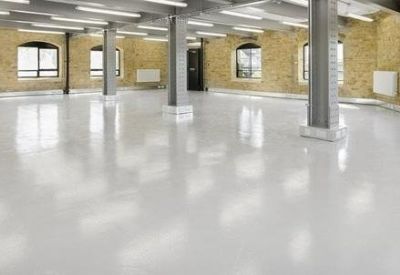 Spacious open-plan office with polished white floors and exposed brick walls.
