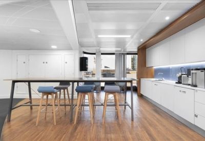 Communal kitchen and breakout area with a high breakfast bar, wooden floors, and modern white cabinetry.