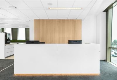 Minimalist white reception desk with a light wood paneled wall behind it.