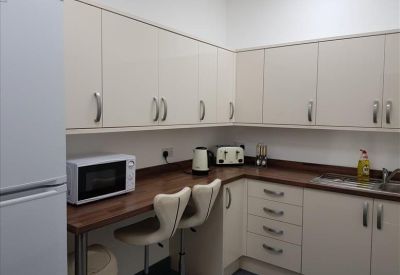 Modern communal kitchen with cream cabinets, wood-effect countertops, and a breakfast bar.