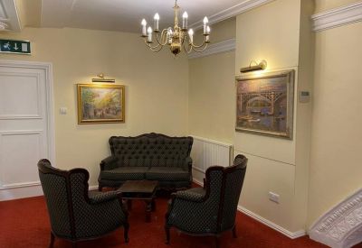 Reception lounge featuring a classic dark leather sofa and armchairs under a chandelier.