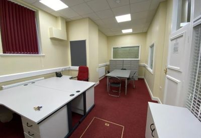 Private office suite with two white desks, a red chair, and natural light from a side window.