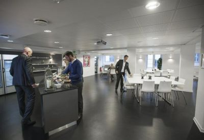 Spacious communal dining area and kitchen with dark flooring and white tables.