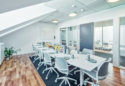 Bright meeting room with a large white table, grey chairs, and a sloped ceiling.