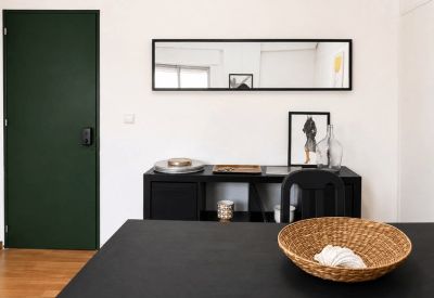Modern reception area featuring a black sideboard, long mirror, and a dark green door.