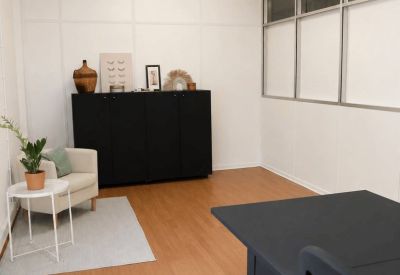 Bright office space with a black storage cabinet, white armchair, and glass-partitioned walls.
