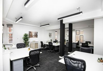 Bright open-plan office space with white desks, black ergonomic chairs, and modern strip lighting.