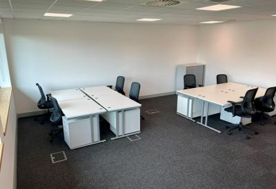 Open-plan workspace featuring several white desks and ergonomic black chairs.