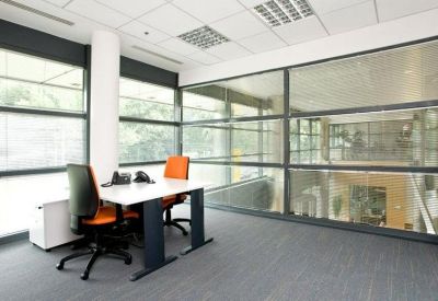 Bright corner office with two workstations and floor-to-ceiling glass partitions.