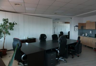 Bright office interior showing workstations and a kitchen area in the background.