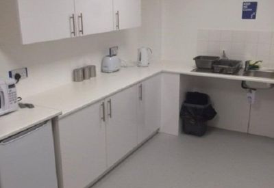 Clean white communal kitchen area with integrated sink, cabinets, and a small fridge.