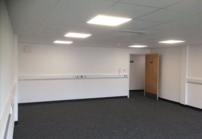 Spacious, empty office room with dark grey carpet and square ceiling lights.
