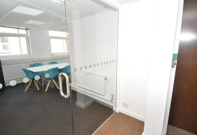 Small meeting room with a white table and teal chairs seen through a glass door.