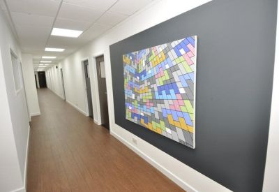 Clean white office corridor with wood-effect flooring and a large colorful geometric artwork.