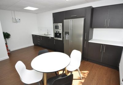 Modern breakroom kitchen with dark wood cabinets and white dining chairs on a wood-effect floor.