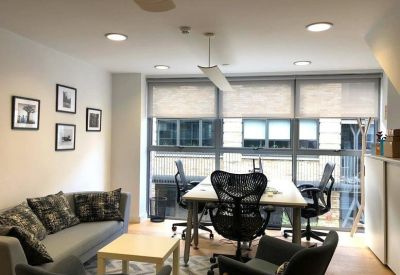 Bright breakout space with grey sofas, a coffee table, and an office desk with ergonomic chairs.