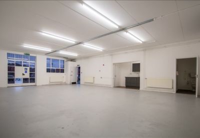 Clean communal area or breakroom with white walls, windows, and a small kitchenette corner.