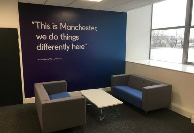 Communal breakout area with a blue feature wall, quote mural, and comfortable grey and blue sofas.