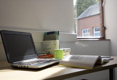 Private office workstation with a laptop and books on a wooden desk near a window.