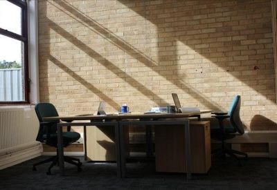 Spacious office with exposed brick walls and two workstations illuminated by natural sunlight.
