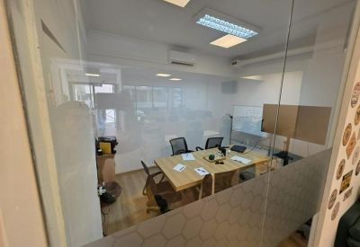 Internal meeting room visible through a glass partition with a light wood table and black chairs.