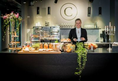 Friendly staff member standing behind a modern reception counter with the building's logo and light refreshments.