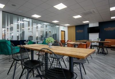 Bright communal breakout area with wooden tables, black mesh chairs, and teal velvet armchairs.