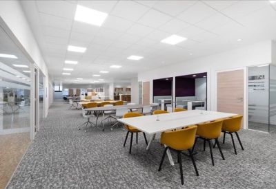 Modern coworking area with a large white table and mustard yellow chairs.