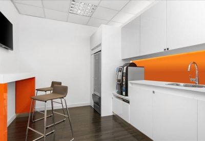 Modern office kitchen and coffee station with a vibrant orange backsplash.