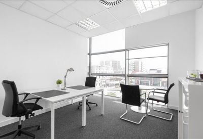 Bright corner office with two white desks and city views through large windows.