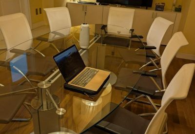 Professional meeting room with a large glass table, white chairs, and video conferencing equipment.