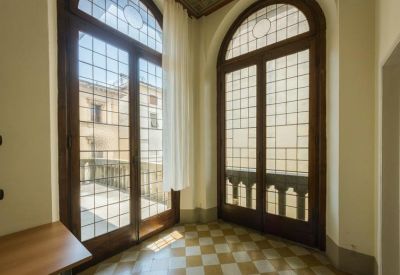 Sunlit interior corner with tall arched windows and checkered tile flooring.