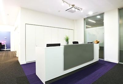 Minimalist reception area with a white desk, purple floor accents, and bright overhead lighting.