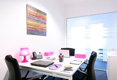 Private office workspace featuring a desk with pink accessories and colorful wall art.