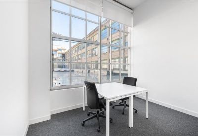 Bright corner office suite with large industrial-style windows and white desks.