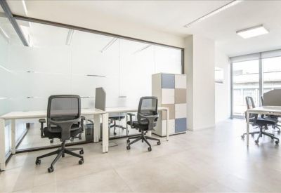 Bright open-plan workspace with white desks and black mesh ergonomic chairs.
