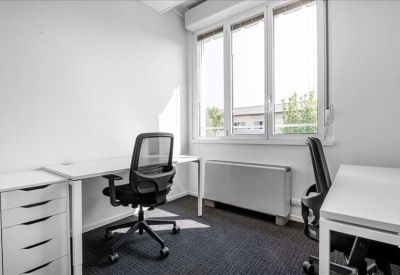 Private office featuring white desks and a grey ergonomic chair by a large window.