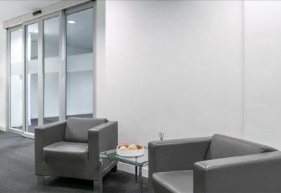 Waiting area featuring two grey leather armchairs and a glass coffee table.