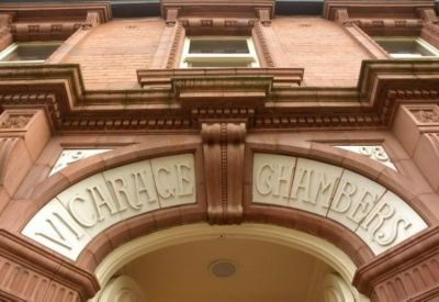 Close-up of the ornate red stone archway with the building name Vicarage Chambers engraved.
