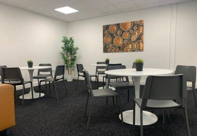 Bright breakout area with circular white tables, grey chairs, and an orange sofa.