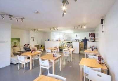 Bright on-site cafe with wooden tables, white chairs, and warm spotlighting.