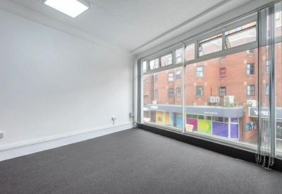 Bright corner office with dark grey carpeting and large windows overlooking the street.