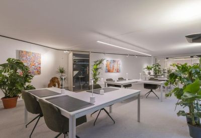 Bright office space featuring L-shaped desks and large leafy potted plants.
