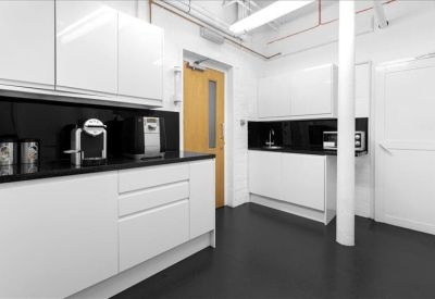 Modern kitchen and breakout area with white cabinetry and sleek black splashback.