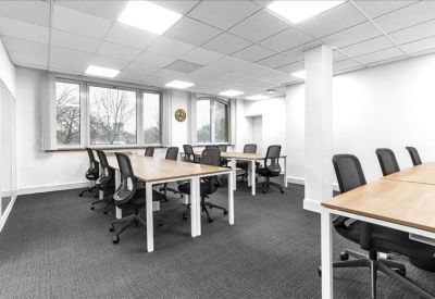 Open-plan office space with light wood desks and ergonomic black chairs.
