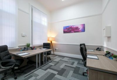 Bright two-person office suite featuring light wood desks, black leather chairs, and a colourful wall art piece.