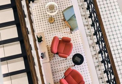 Overhead view of a breakout space with red armchairs and patterned tiling seen through a decorative staircase railing.